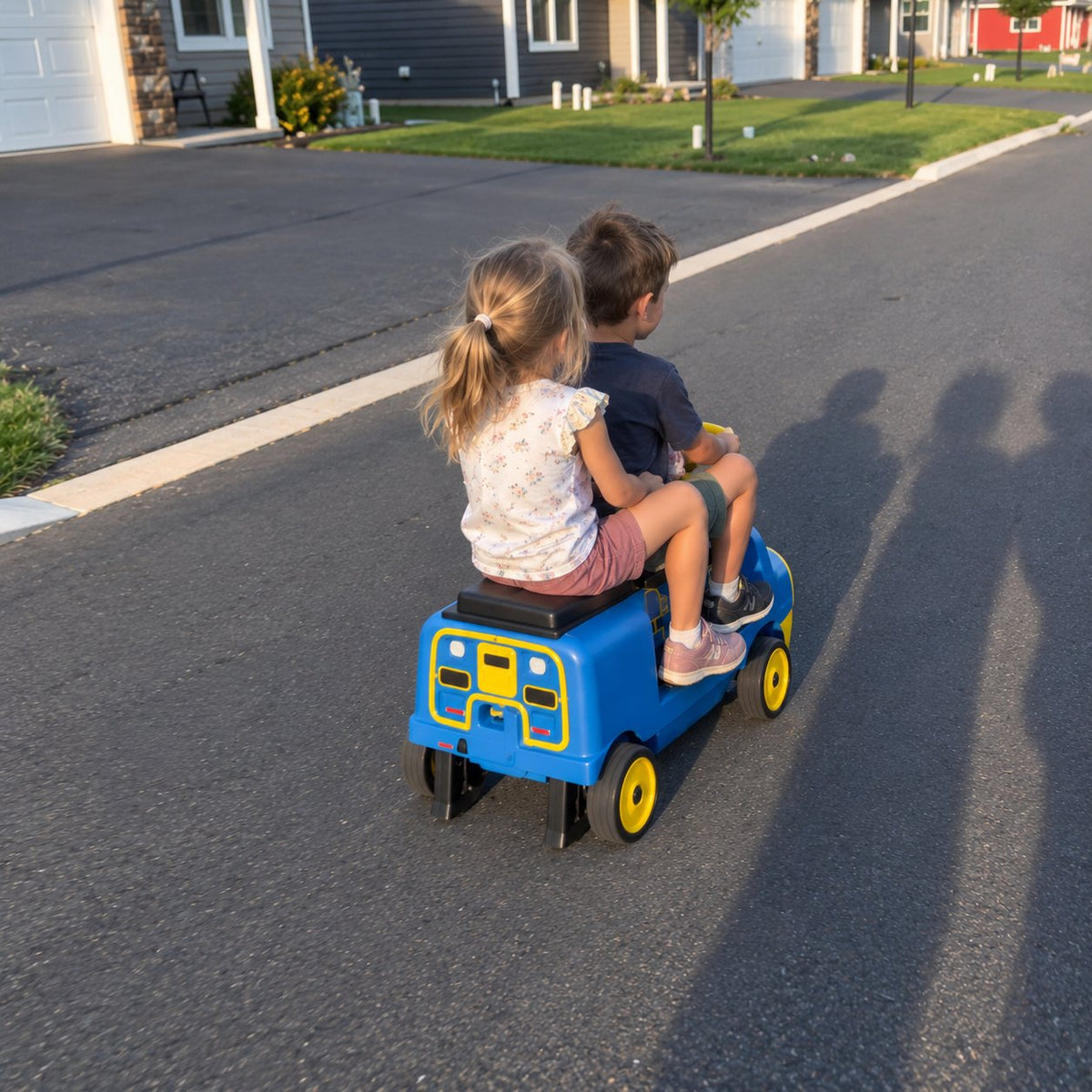 Two kids riding the blue ELEMARA Chuggington ride-on train down the driveway at sunset