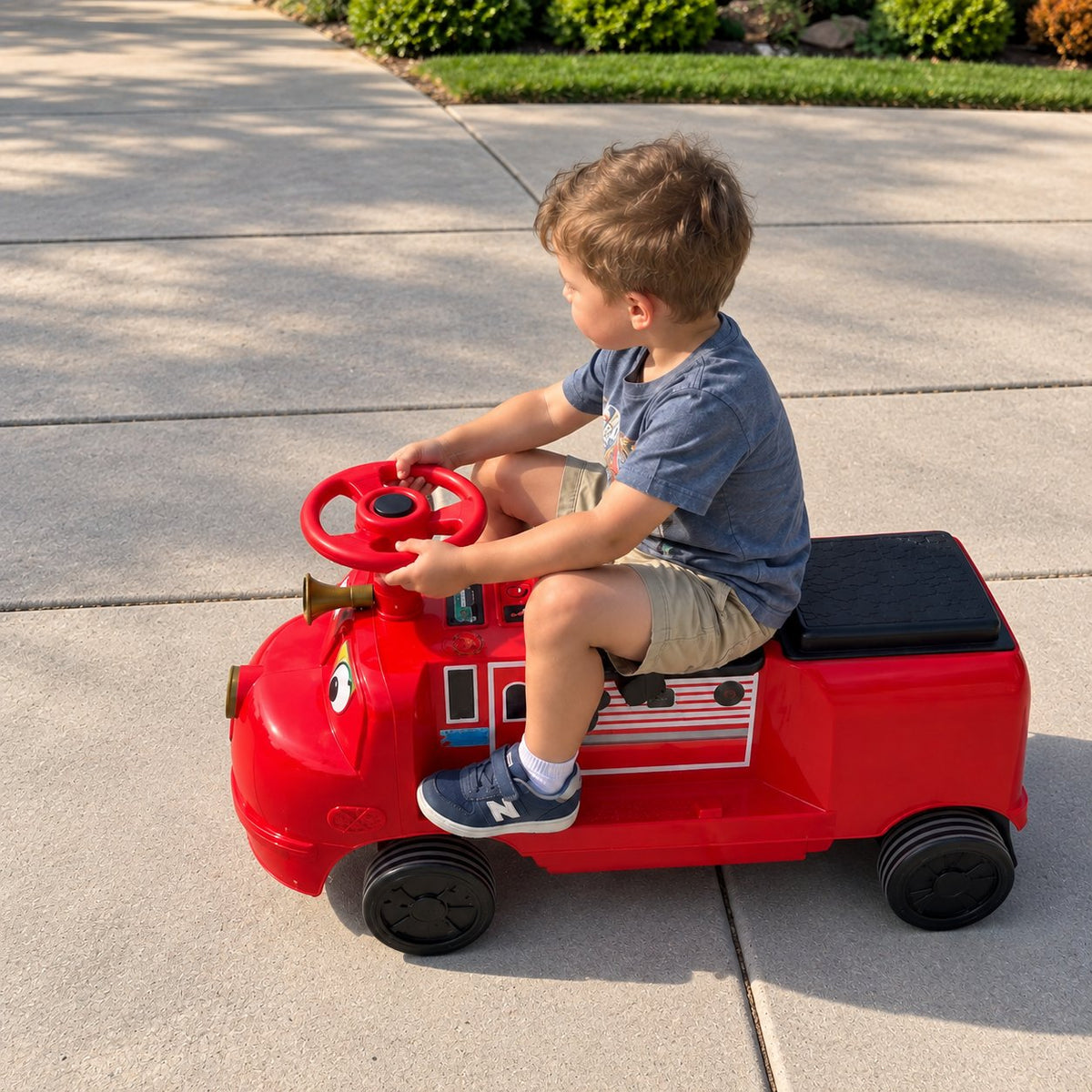 A child riding the red ELEMARA Chuggington ride-on train along a sunny sidewalk